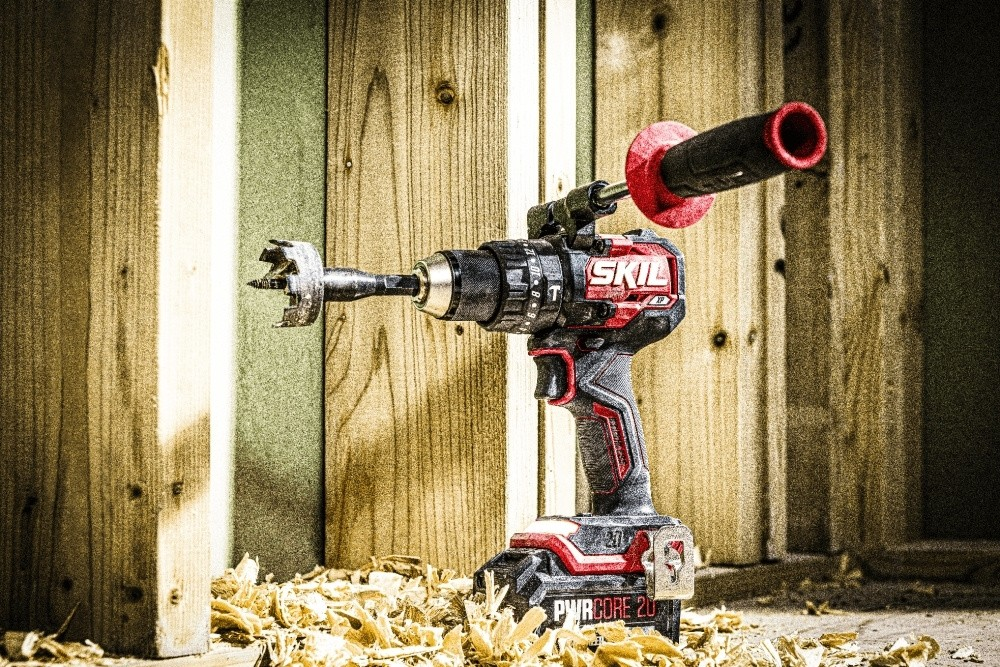 Un trapano a batteria Skil rosso e nero si trova davanti a montanti in legno.