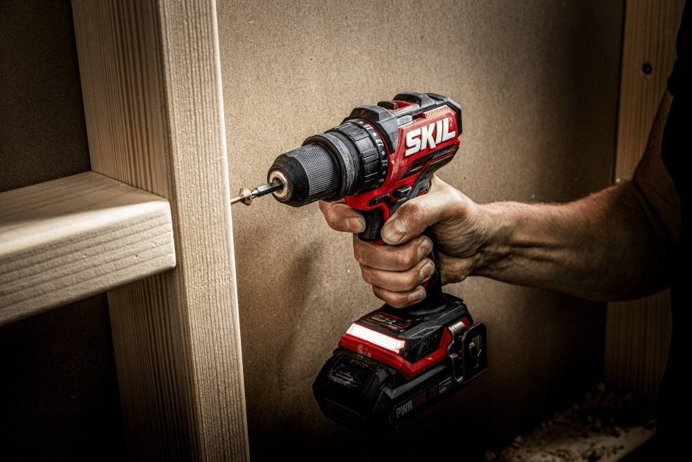 Una mano tiene un trapano a batteria Skil rosso che avvita nel legno.