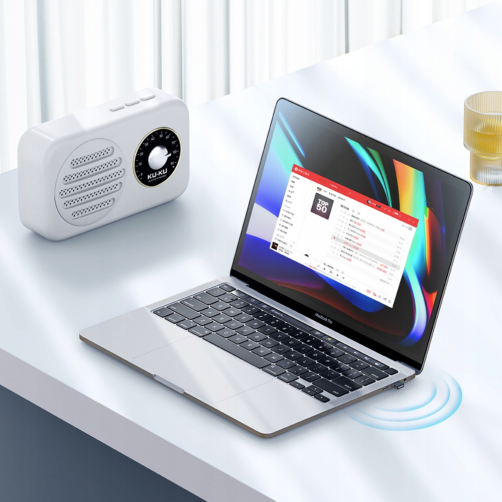 Un computer portatile argentato, un altoparlante bianco e una tazza gialla si trovano su una scrivania bianca.
