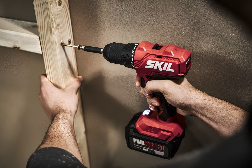 Una persona usa un trapano a batteria SKIL rosso per avvitare una trave di legno.