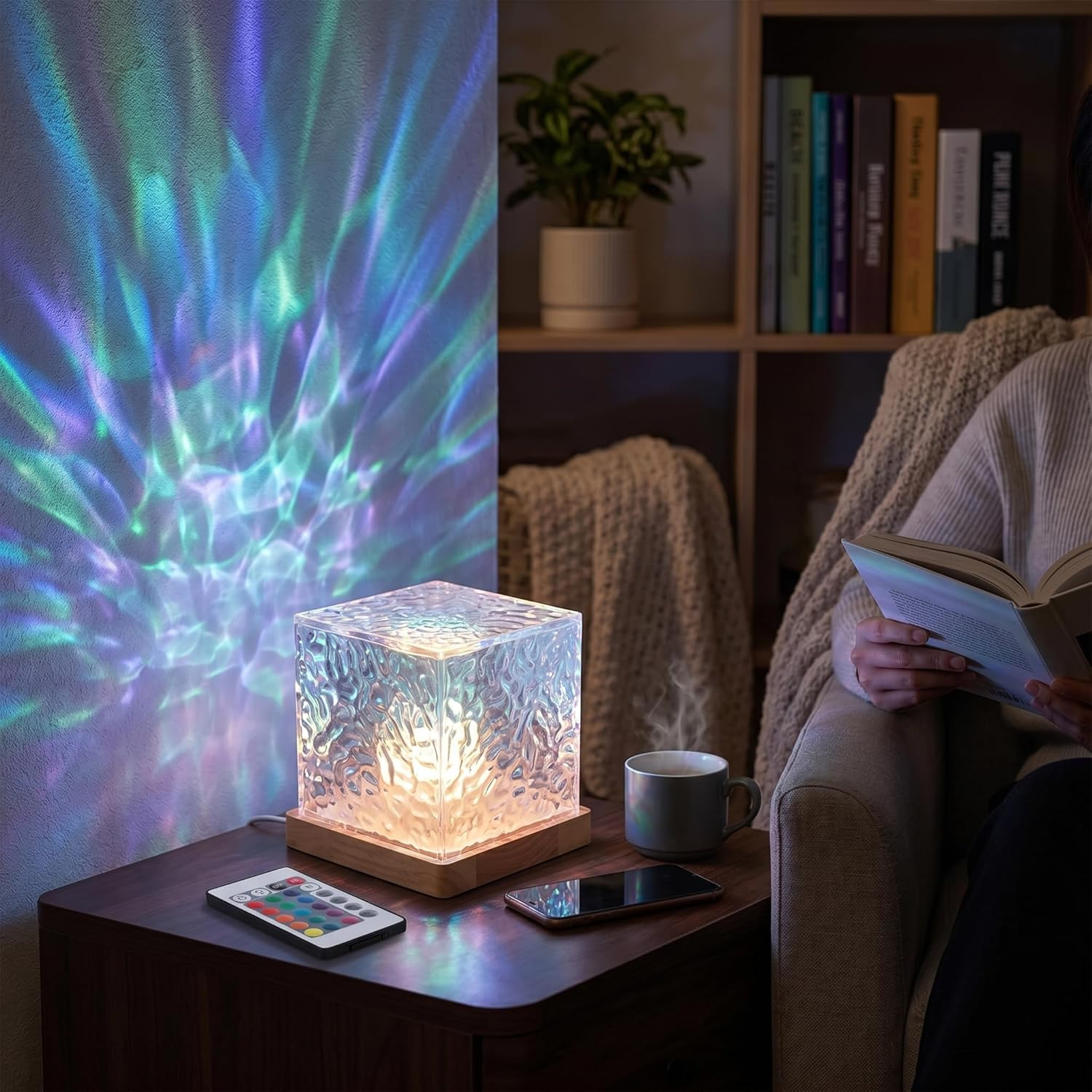 Eine Würfellampe auf einem Tisch projiziert farbige Lichter an eine Wand, während jemand ein Buch liest.