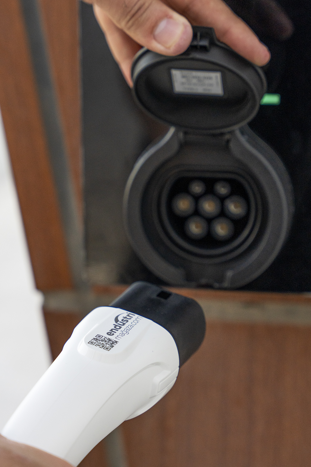 Bir el, beyaz bir konnektör tutarken siyah bir elektrikli araç şarj soketini açıyor.