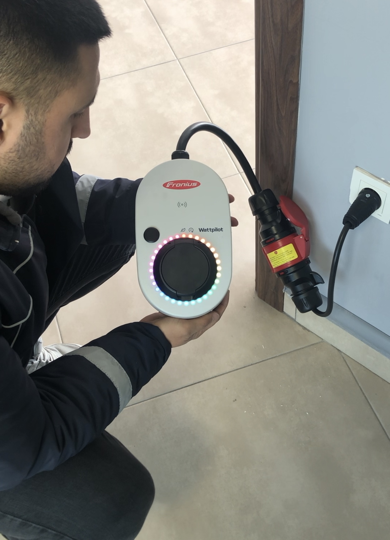 Bir teknisyen, kırmızı sanayi tipi fişe bağlı bir Fronius Wattpilot EV şarj cihazı tutuyor.