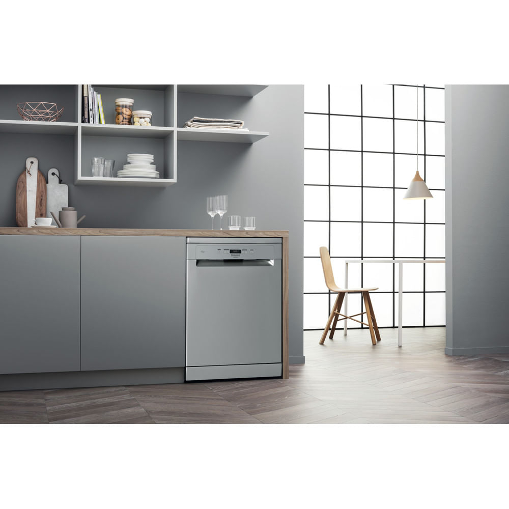 Cucina moderna con lavastoviglie argentata, piano di lavoro in legno, mobili grigi e grande finestra a griglia sullo sfondo.