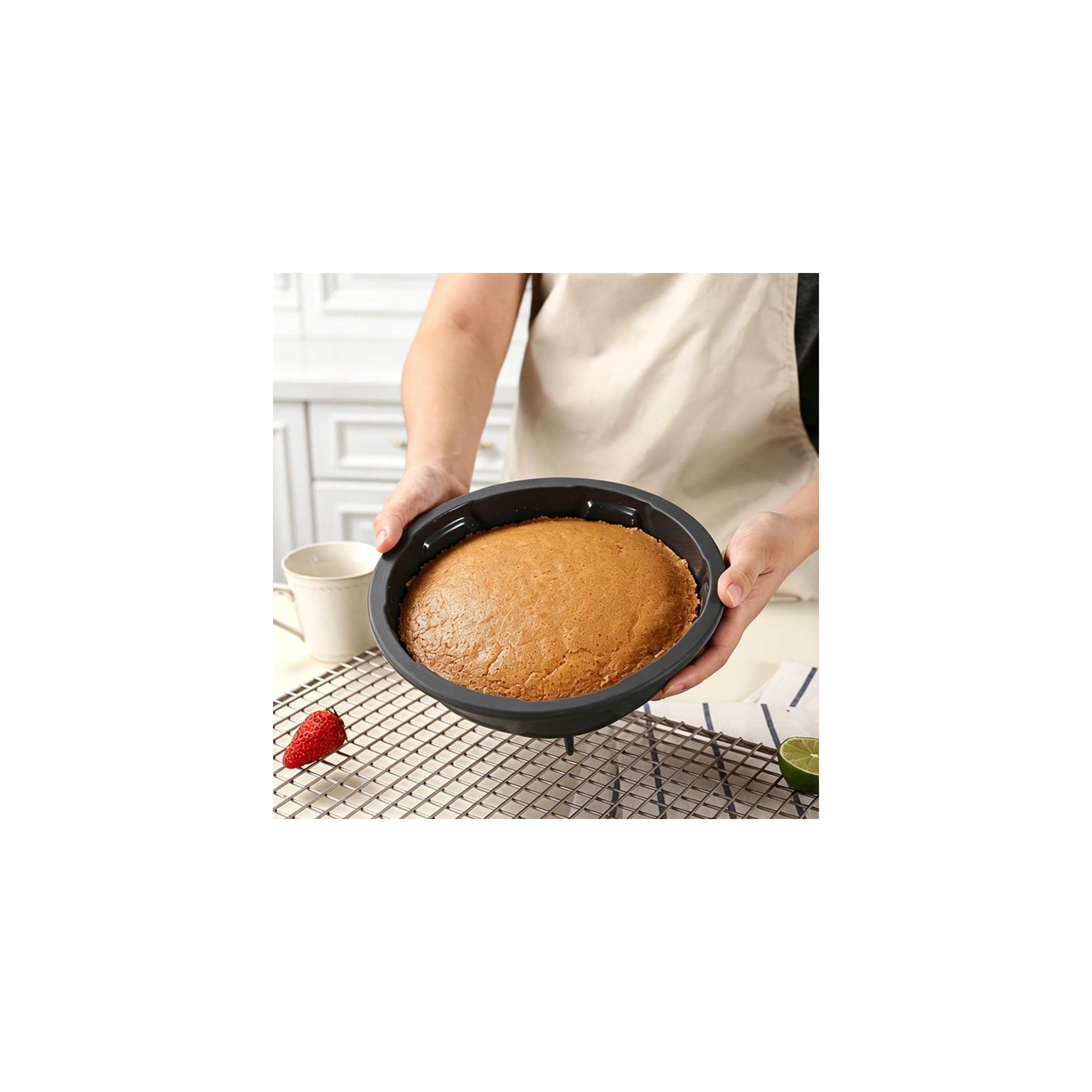 Person in Schürze hält einen runden Kuchen in einer Silikonform über einem Gitter.
