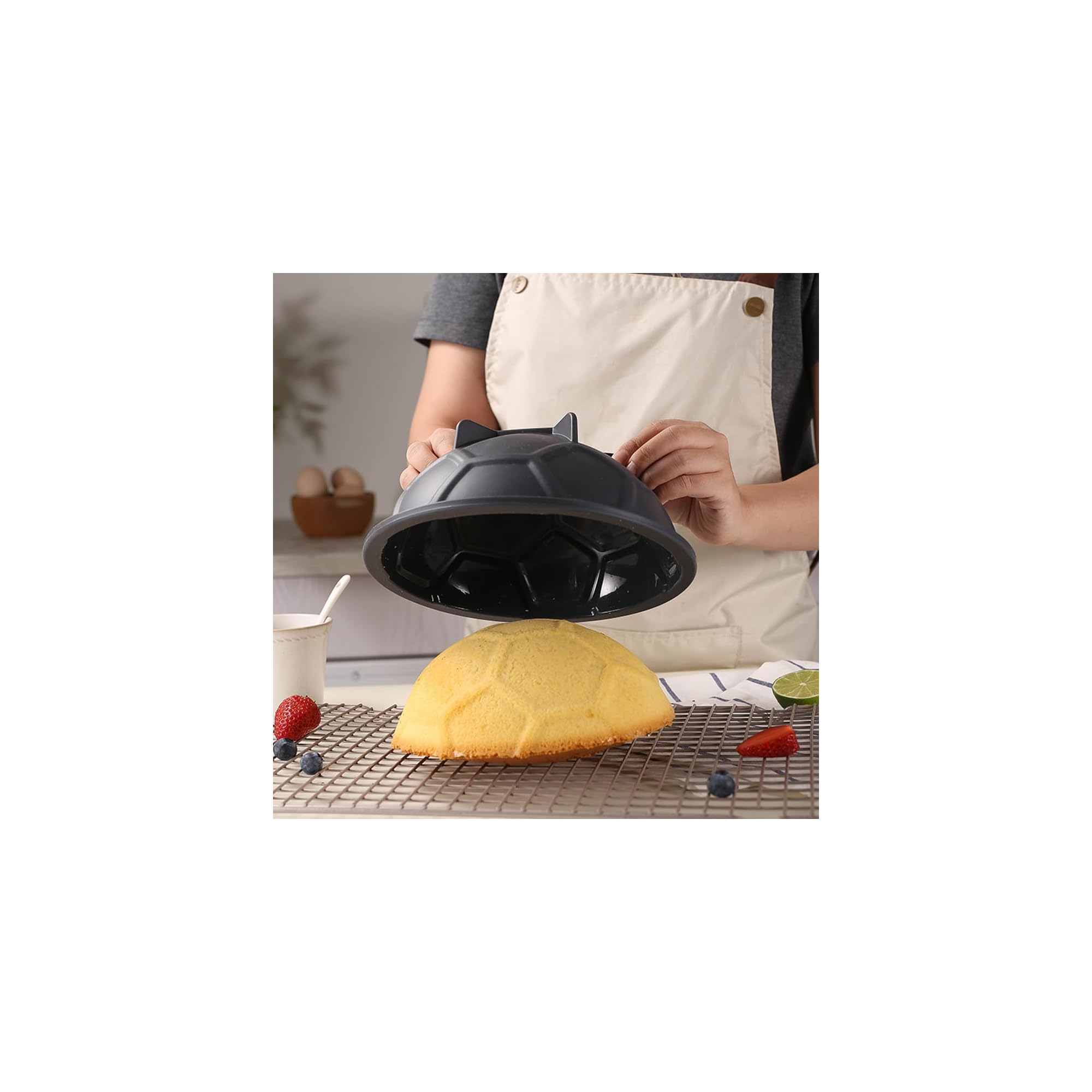 Eine Person hebt eine graue Silikon-Kuchenform von einem fertig gebackenen, fußballförmigen Kuchen ab.