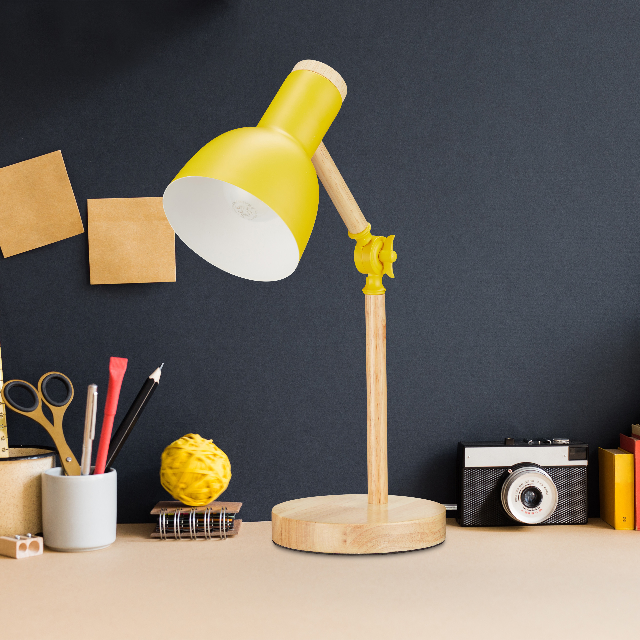 Eine gelbe Schreibtischlampe aus Holz und Metall steht auf einem Tisch neben einer Kamera und Notizen.
