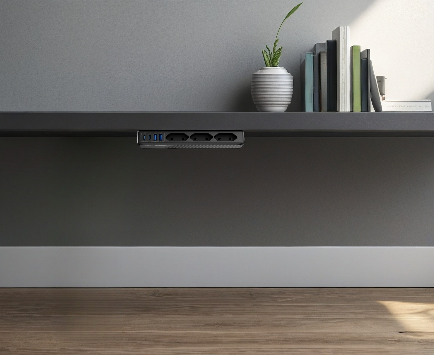 Eine Steckdosenleiste mit USB-Ports ist unter einem grauen Tisch montiert. Auf dem Tisch stehen Bücher und eine Pflanze.