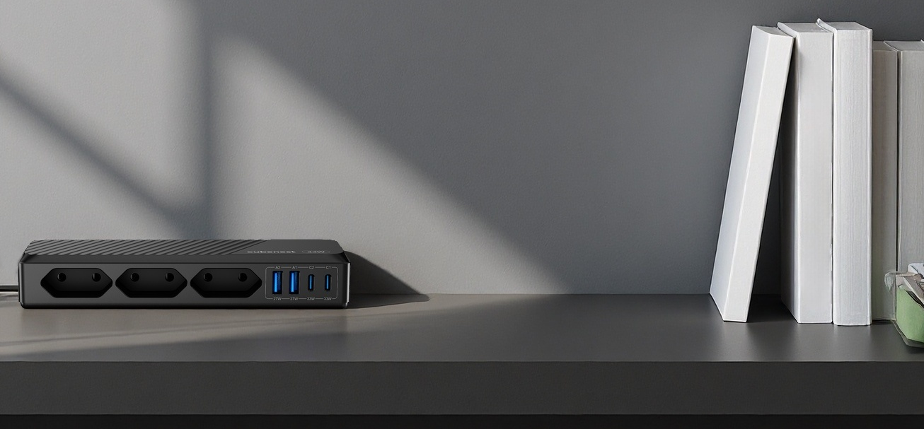 Eine schwarze Steckdosenleiste mit USB-Anschlüssen steht neben weißen Büchern auf einem Regal.
