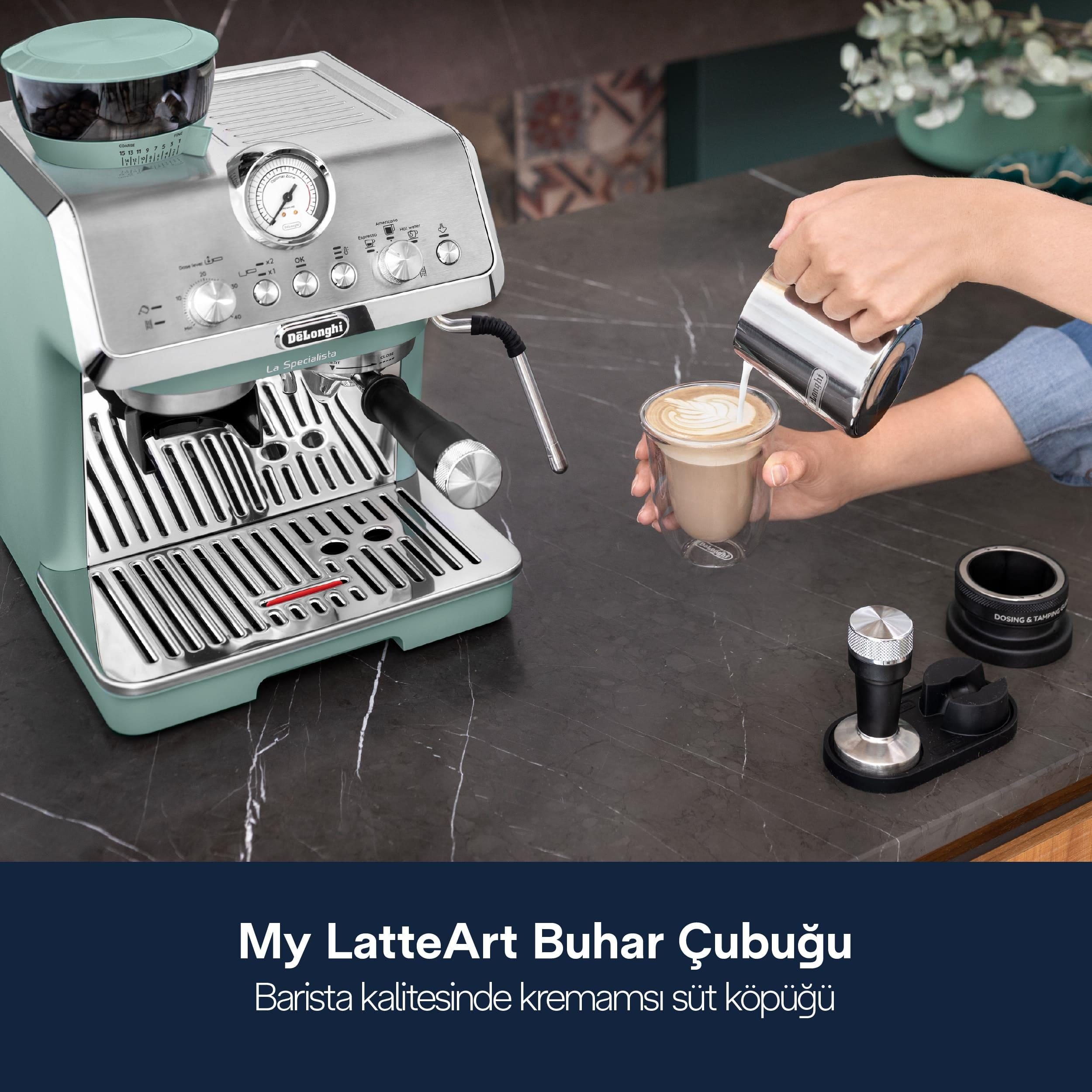 Nane yeşili bir espresso makinesinin yanında metal bir sürahiden kahve bardağına süt döken bir kişi.