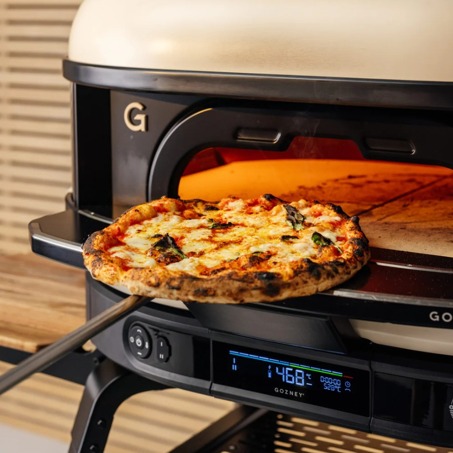 Eine frische Pizza auf einer Schaufel vor einem modernen, heißen Pizzaofen.