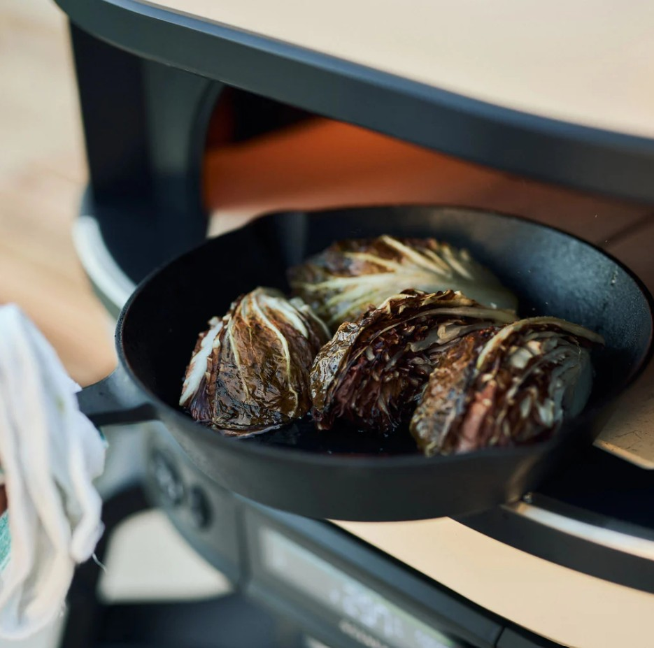 Eine Gusseisenpfanne mit gegrillten Radicchio-Vierteln wird vor einem Pizzaofen gehalten.