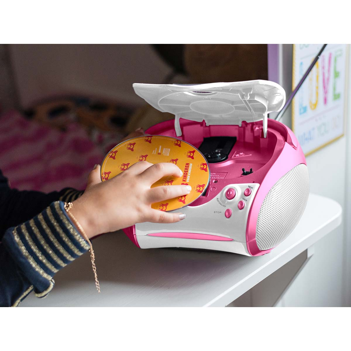 Un bambino inserisce un CD arancione in uno stereo rosa e bianco su un tavolo.