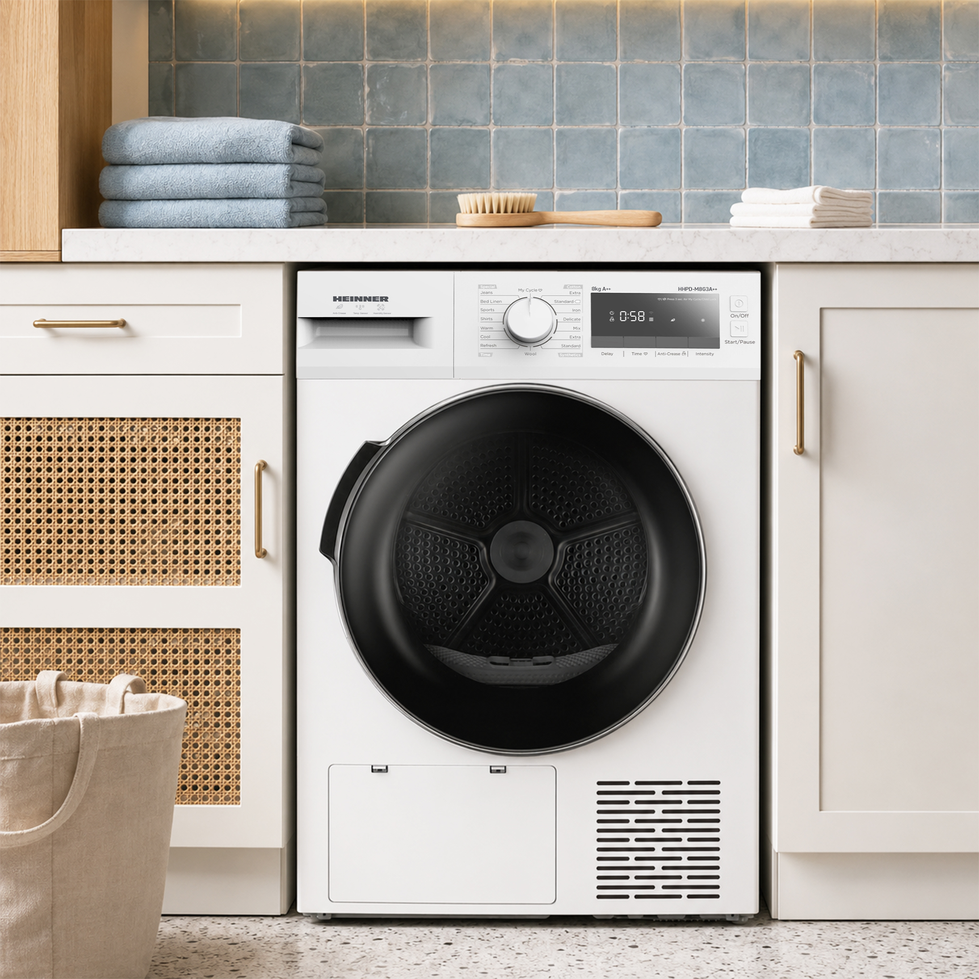 White Heinner tumble dryer in a laundry room with blue tiles, folded towels, and a laundry basket.