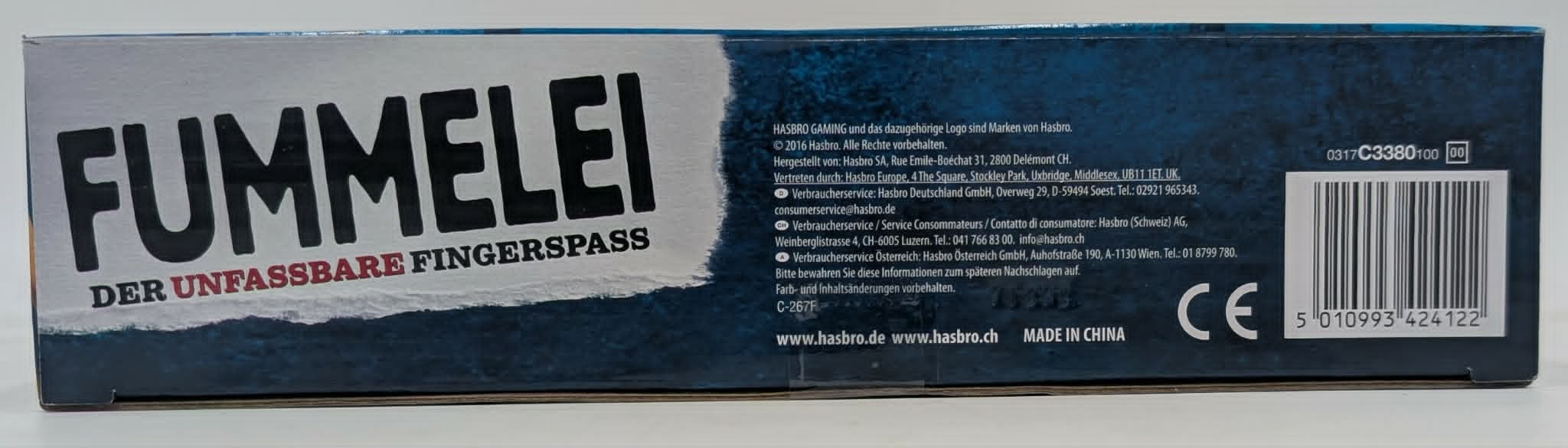 Verpackung des Spiels "Fummelei" mit Text, Herstellerinfos, CE-Zeichen und Barcode auf blauem Hintergrund.