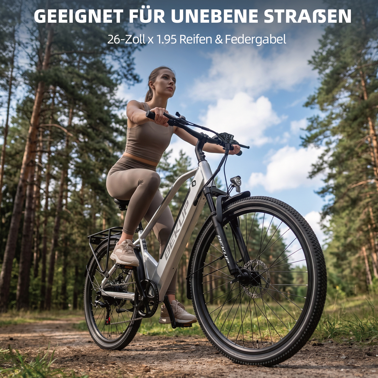 Eine Frau fährt ein silbernes E-Bike auf einem Waldweg, umgeben von Bäumen und blauem Himmel.