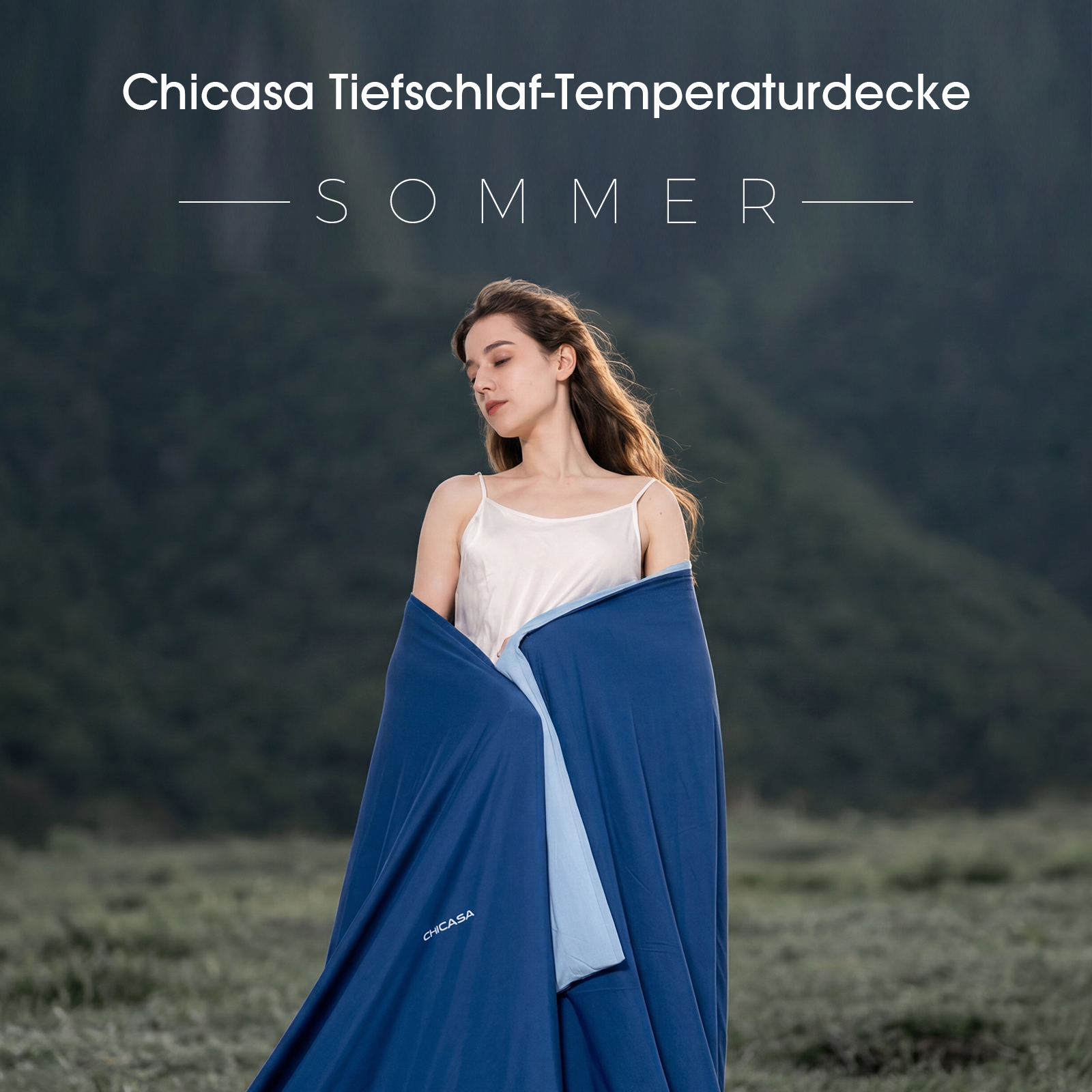 Eine Frau in weißem Top steht im Freien und ist in eine blaue Chicasa-Decke gewickelt.
