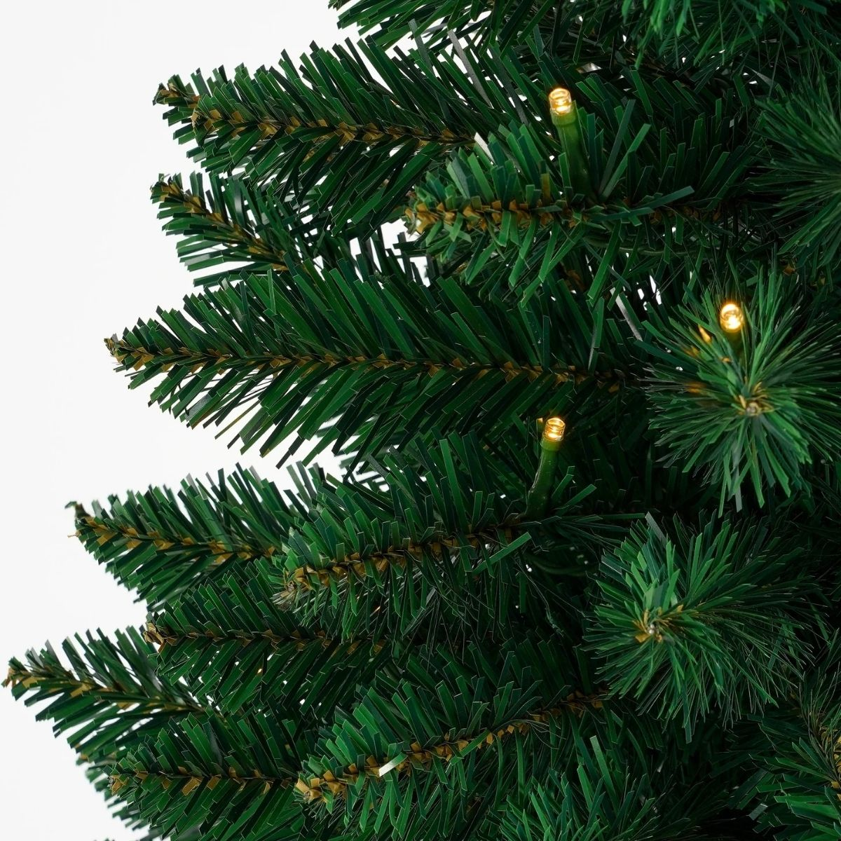 Nahaufnahme von künstlichen grünen Weihnachtsbaumzweigen mit kleinen warmweißen Lichtern.
