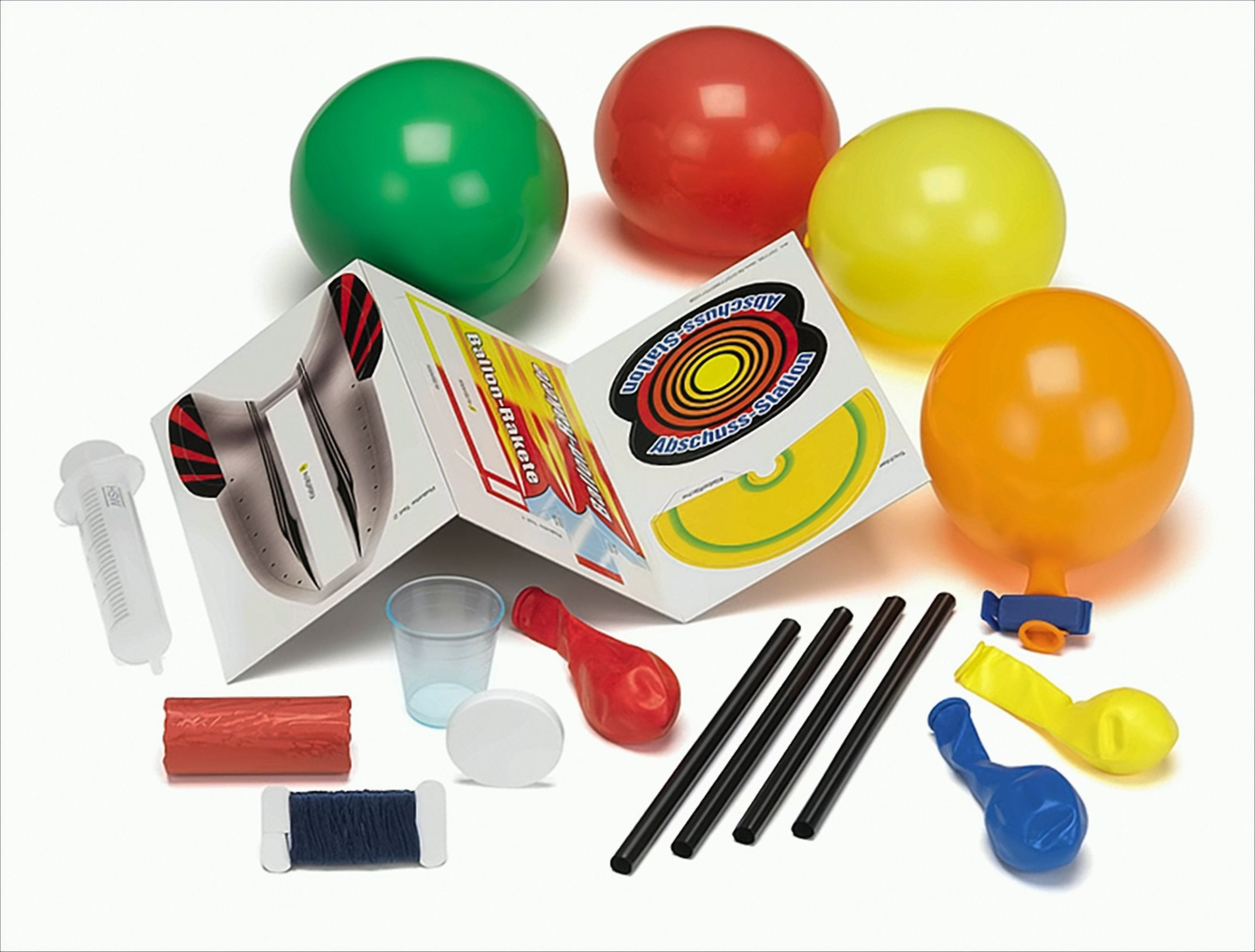 Wissenschaftsset mit farbigen Ballons, Anleitung, Plastikbecher, Spritze, Strohhalmen und Garn auf weißem Grund.