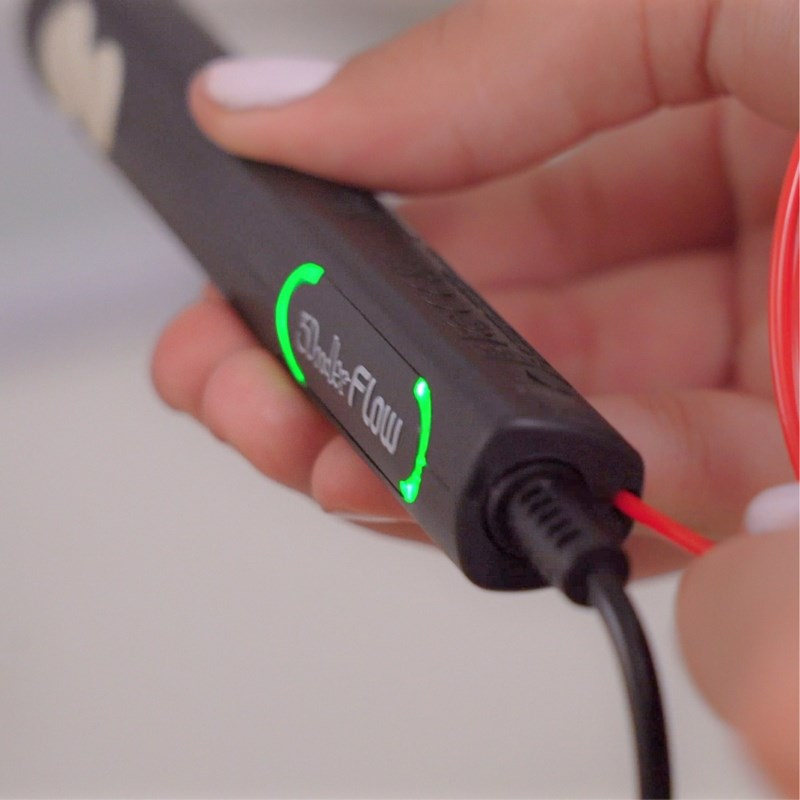 Una mano sostiene un lápiz 3D negro con un indicador verde brillante y un cable conectado.