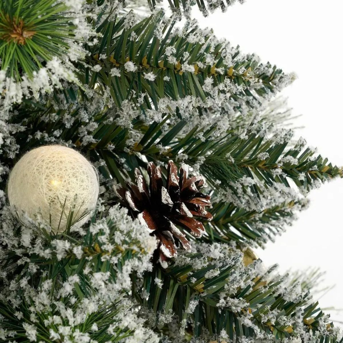 Verschneiter Weihnachtsbaum mit Tannenzapfen und einer weißen Lichterkugel.