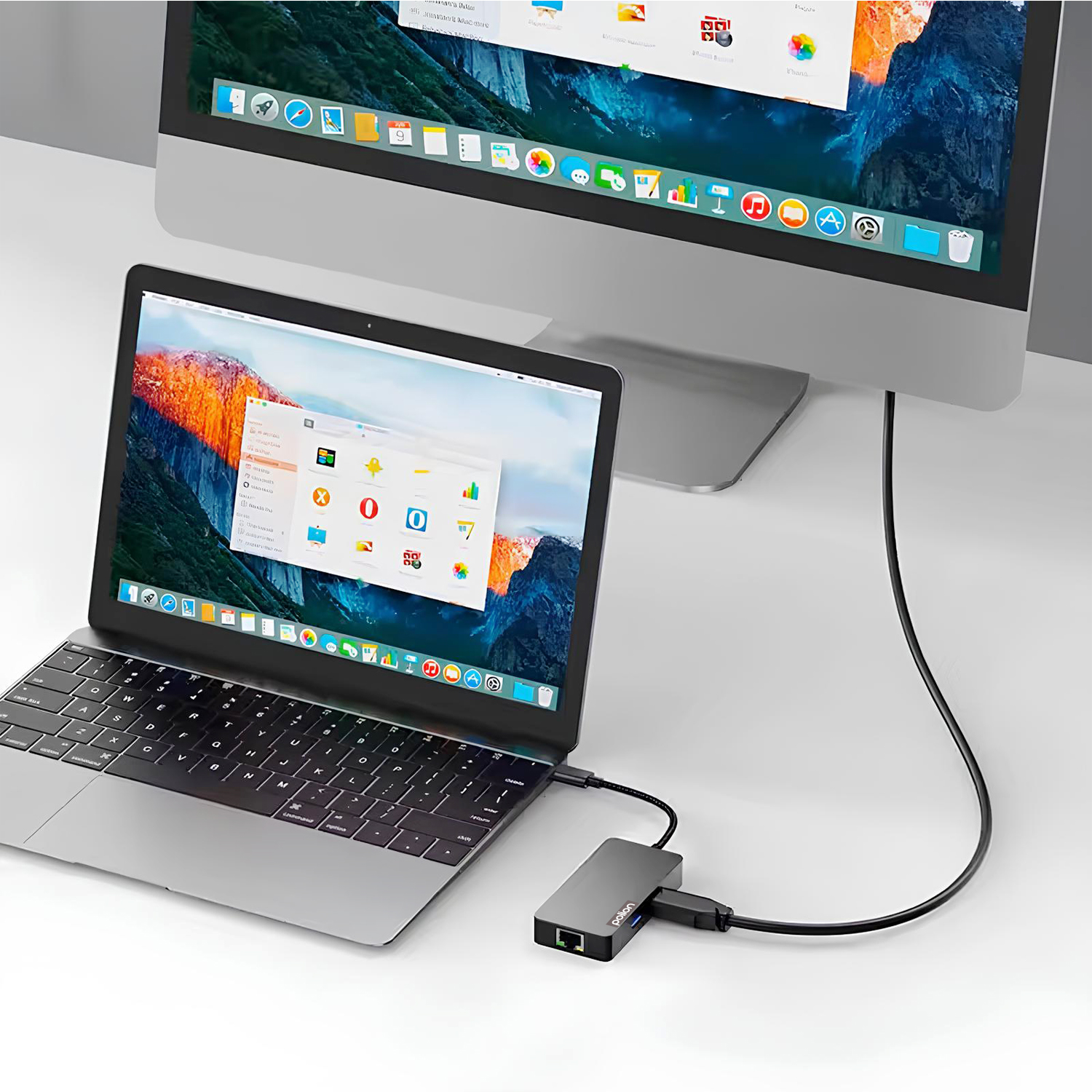 Laptop podłączony przez hub do dużego monitora na białym biurku.