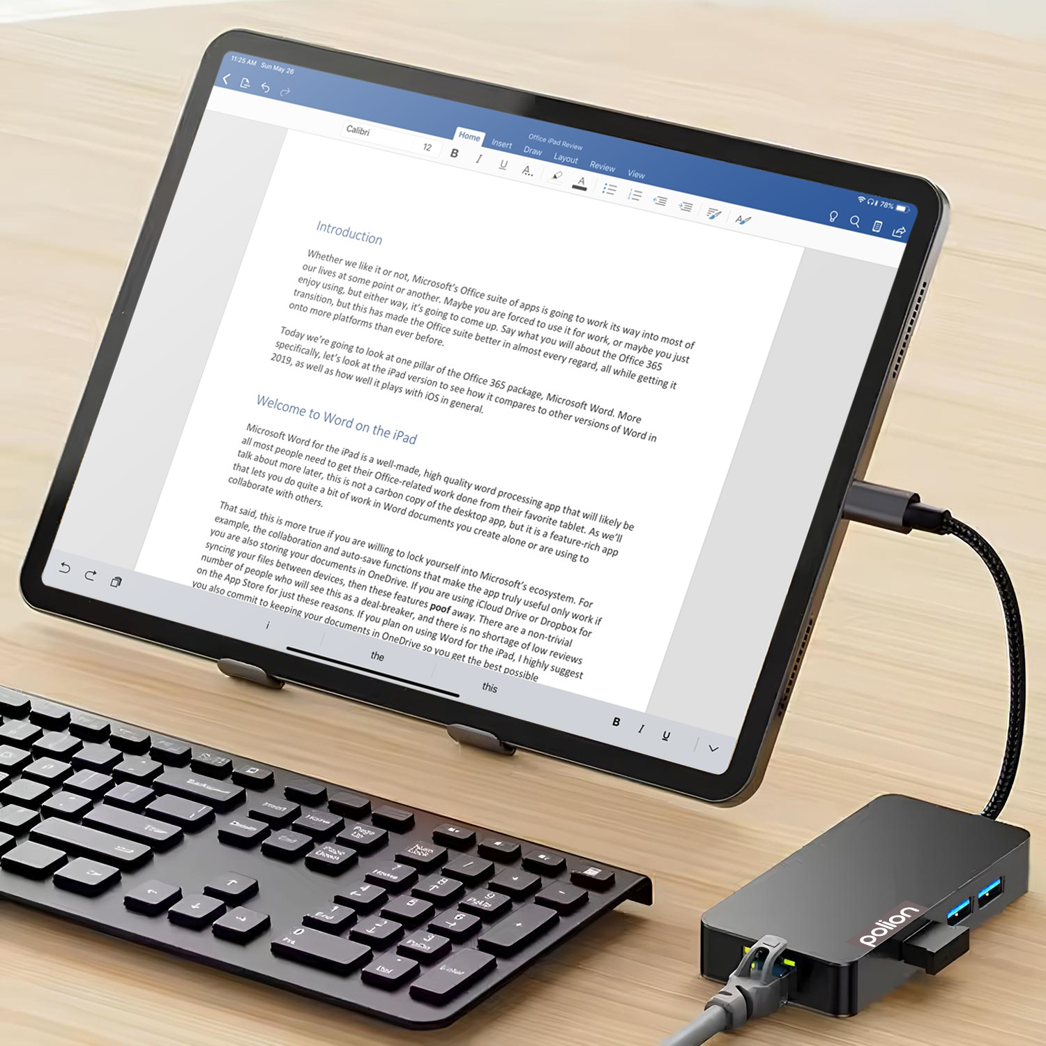Tablet na stojaku z podłączoną klawiaturą i hubem USB, wyświetlający dokument na drewnianym biurku.