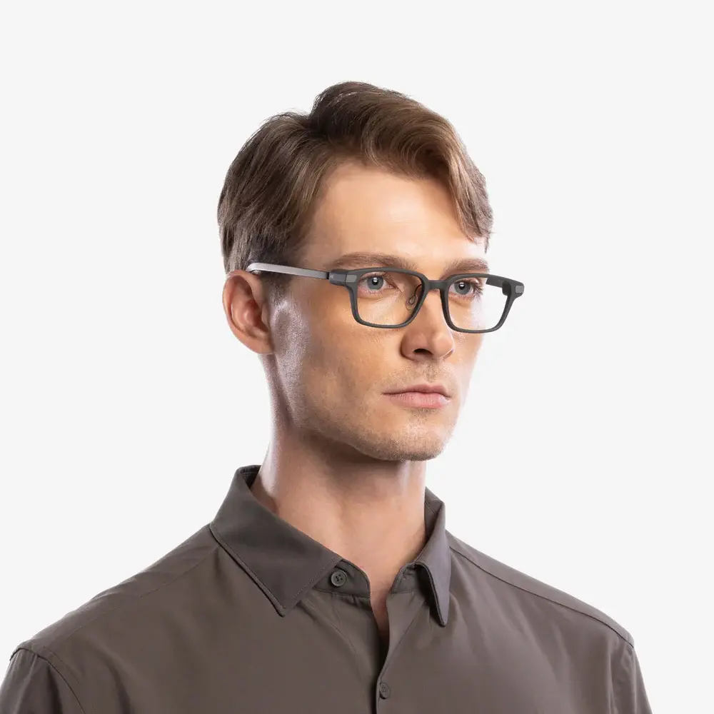 Un hombre con gafas gris oscuro y camisa gris oscuro con cuello sobre fondo blanco.