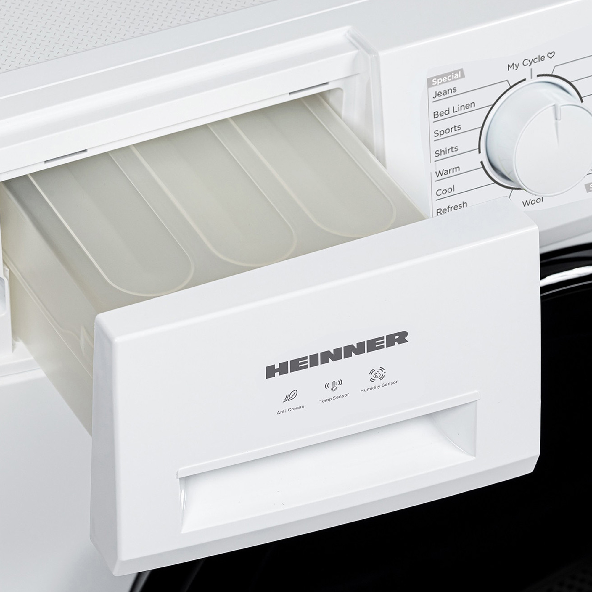 A white Heinner washing machine with its detergent drawer pulled out, showing the internal plastic compartments.