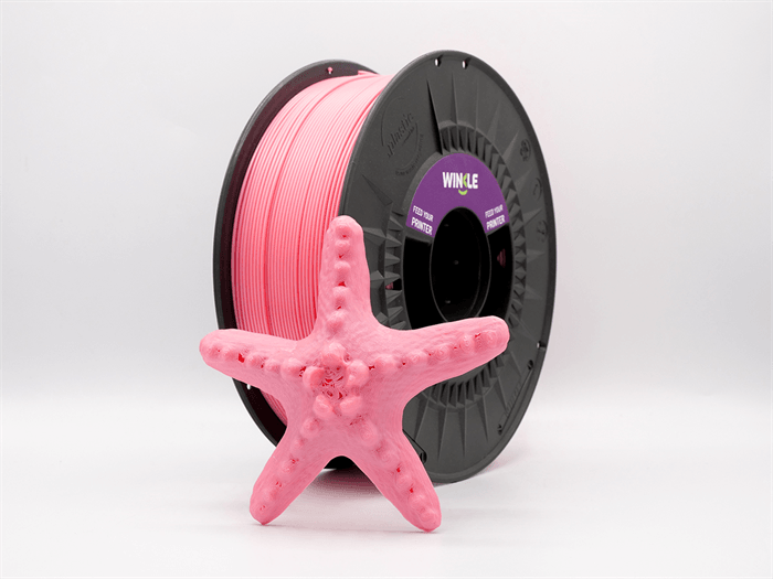 Una stella marina rosa stampata in 3D si trova davanti a una bobina di filamento.