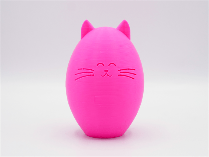 Una statuetta di gatto rosa stampata in 3D con corpo rotondo, orecchie appuntite e viso felice su sfondo bianco.