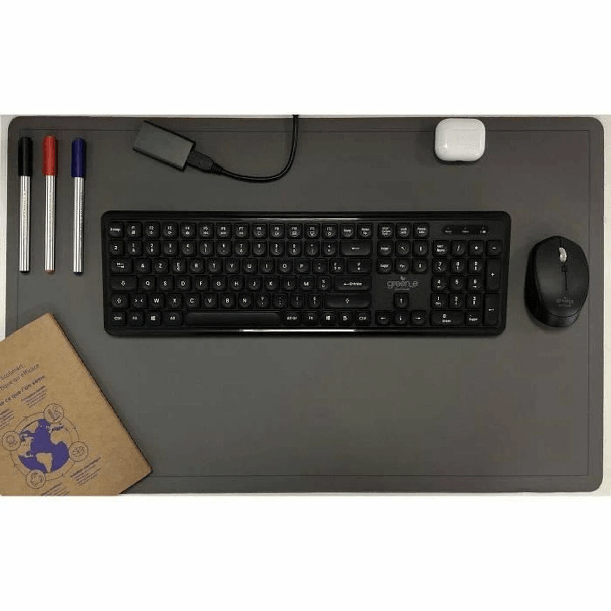 Tastiera e mouse neri su sottomano grigio, con tre penne, adattatore USB, auricolari e taccuino.
