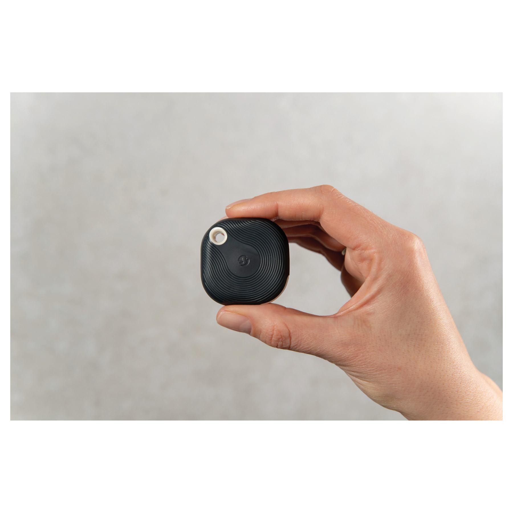 Una mano tiene un piccolo localizzatore quadrato nero con superficie scanalata e foro bianco.