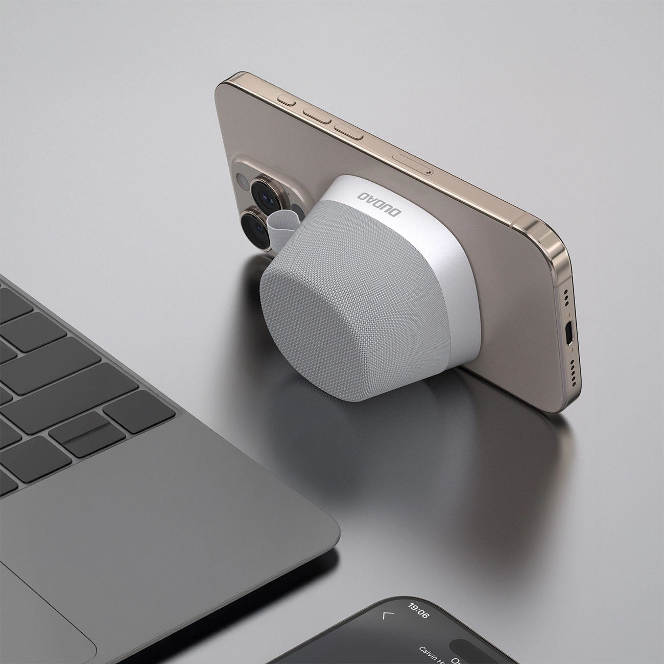 Un altoparlante magnetico grigio Dudao attaccato al retro di uno smartphone dorato su una scrivania.