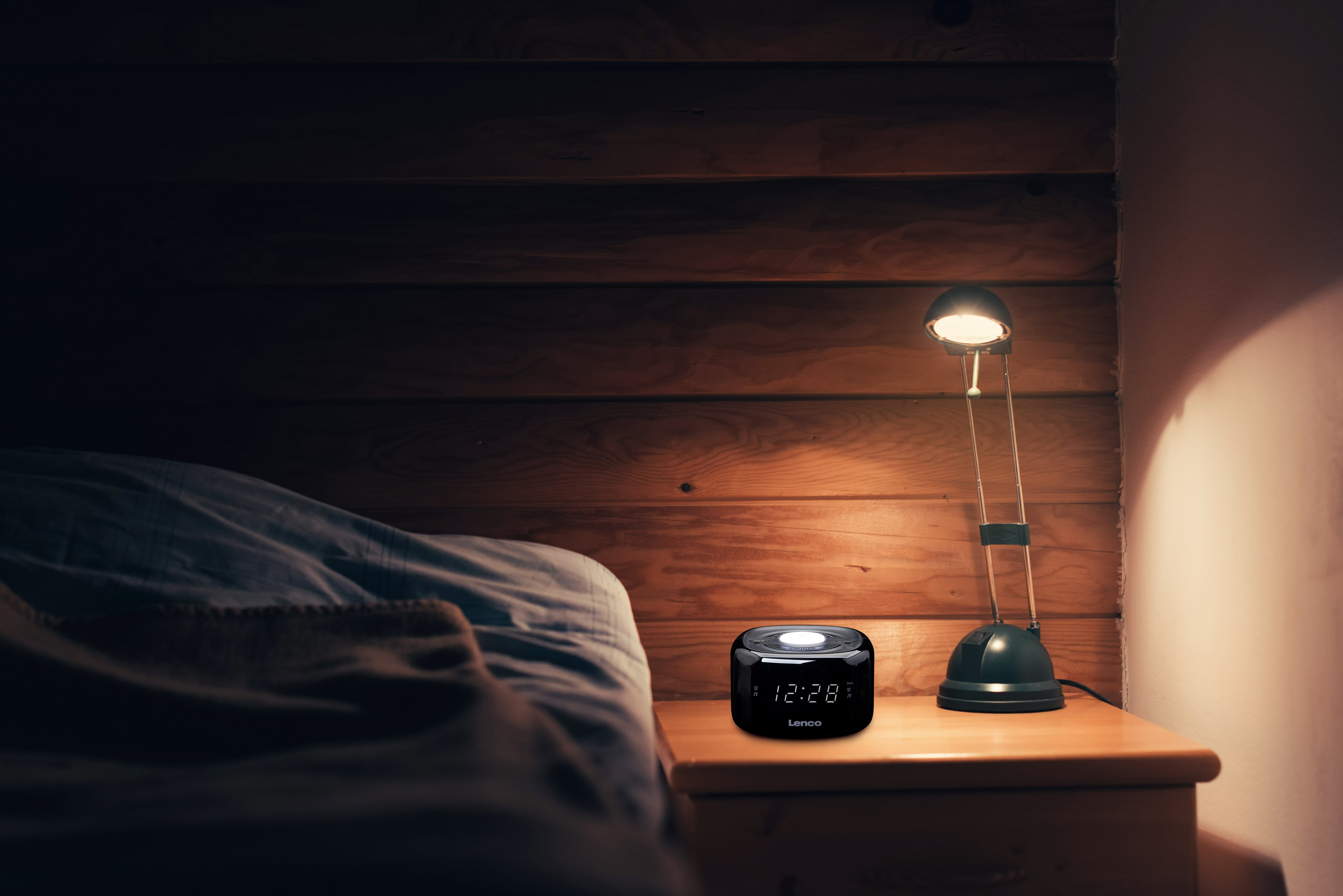 Un comodino con una lampada e un orologio accanto a un letto contro una boiserie.