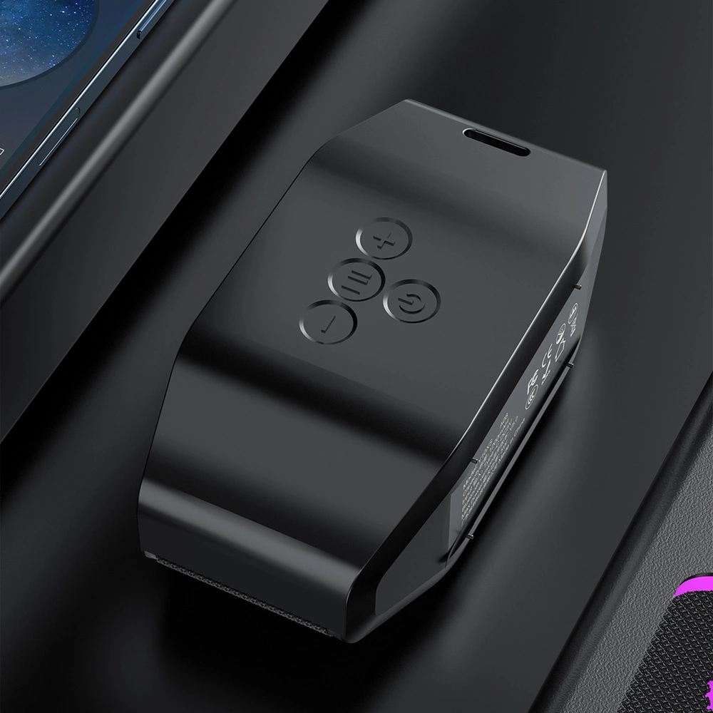 Un gadget nero e allungato con quattro pulsanti superiori poggia su una superficie scura accanto a uno smartphone.