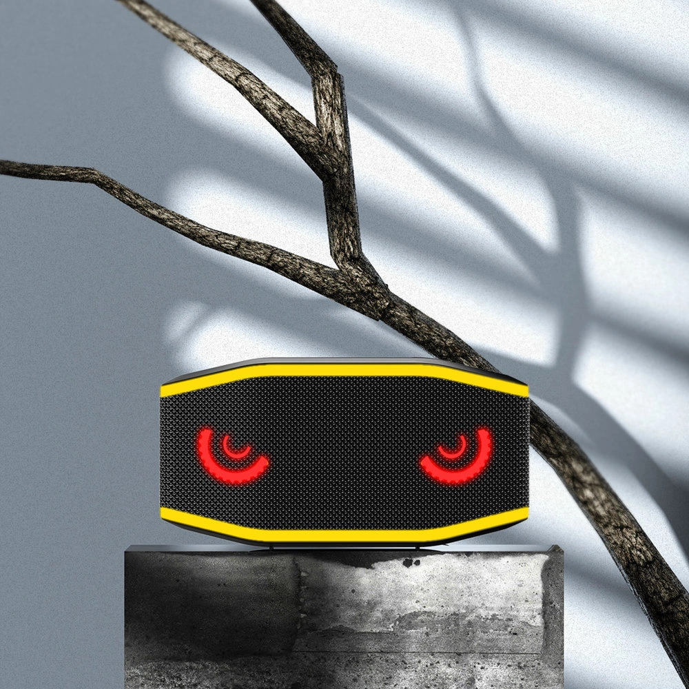 Un altoparlante giallo con occhi rossi luminosi su un piedistallo davanti a un ramo e muro grigio.