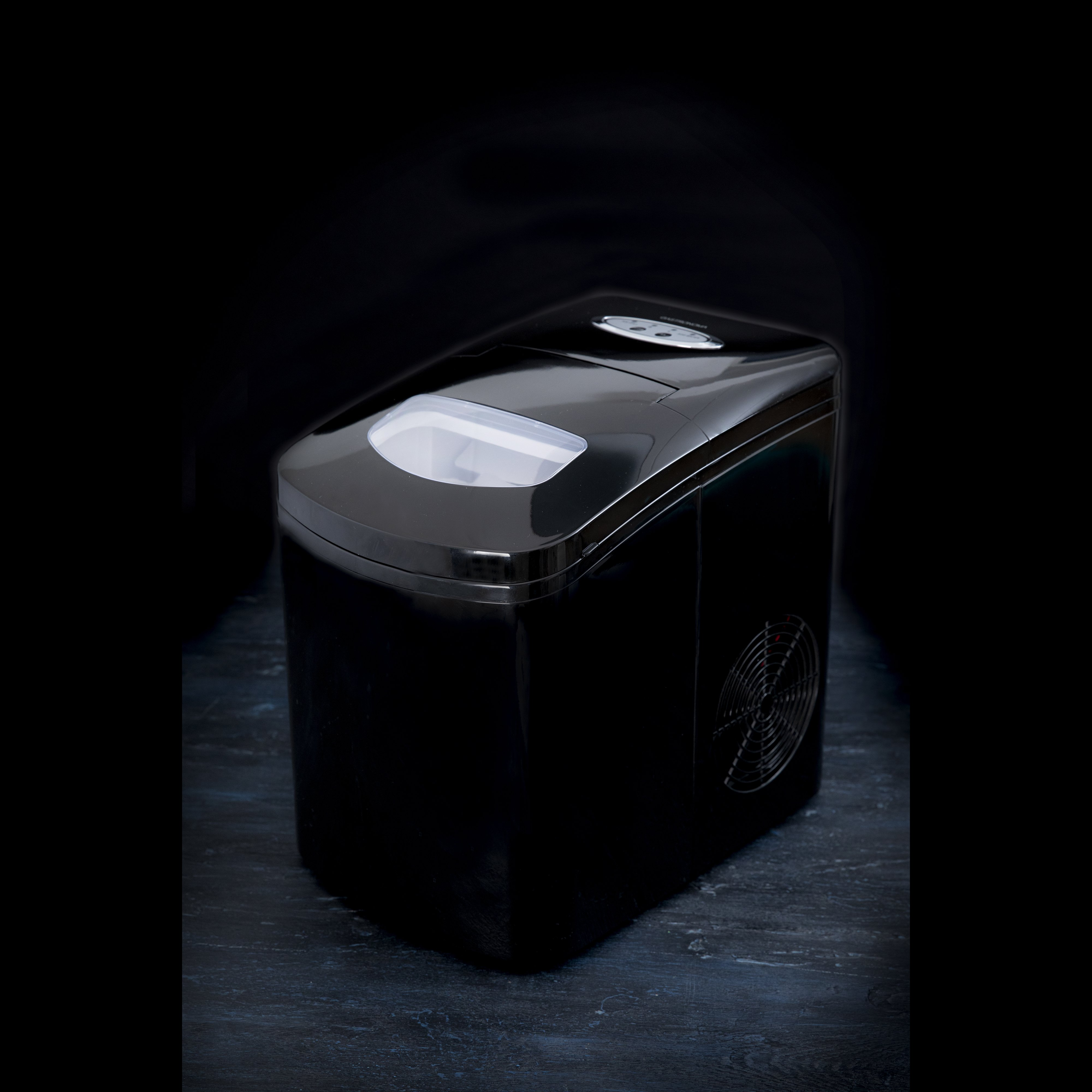 Une machine à glaçons noire et compacte sur une surface sombre avec fond noir.