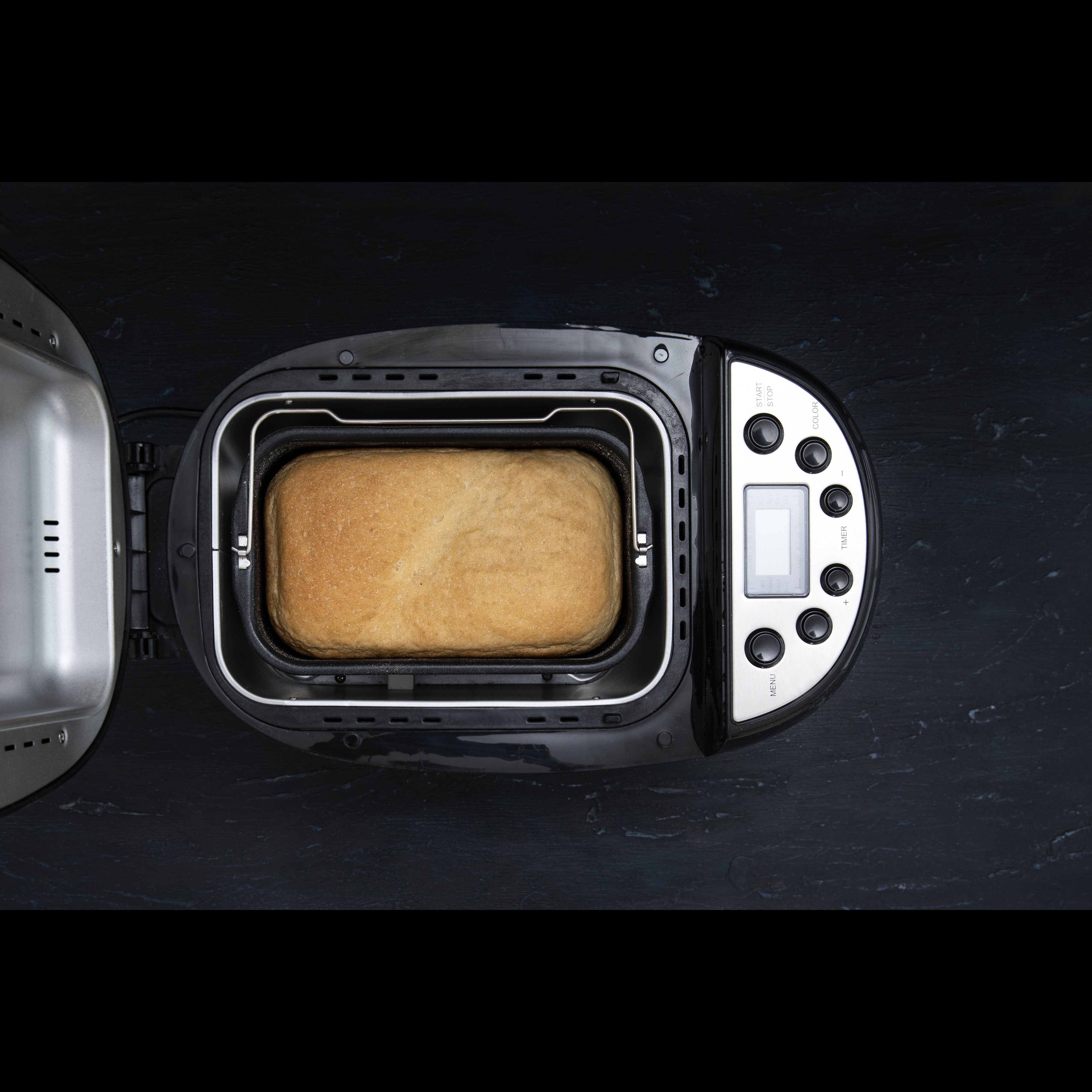 Top-Ansicht eines modernen Brotbackautomaten mit frisch gebackenem Brot innen auf schwarzem Hintergrund.