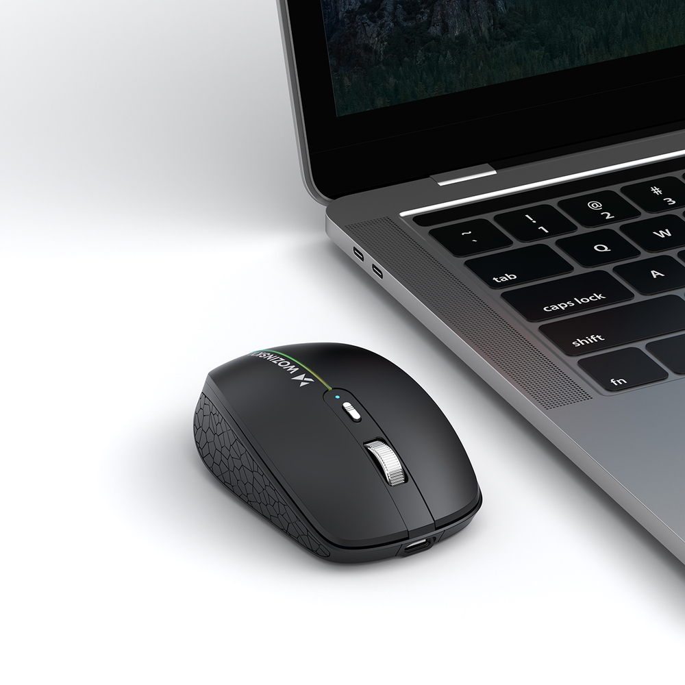 Un mouse wireless nero con impugnatura testurizzata si trova su una superficie bianca accanto a un laptop grigio.