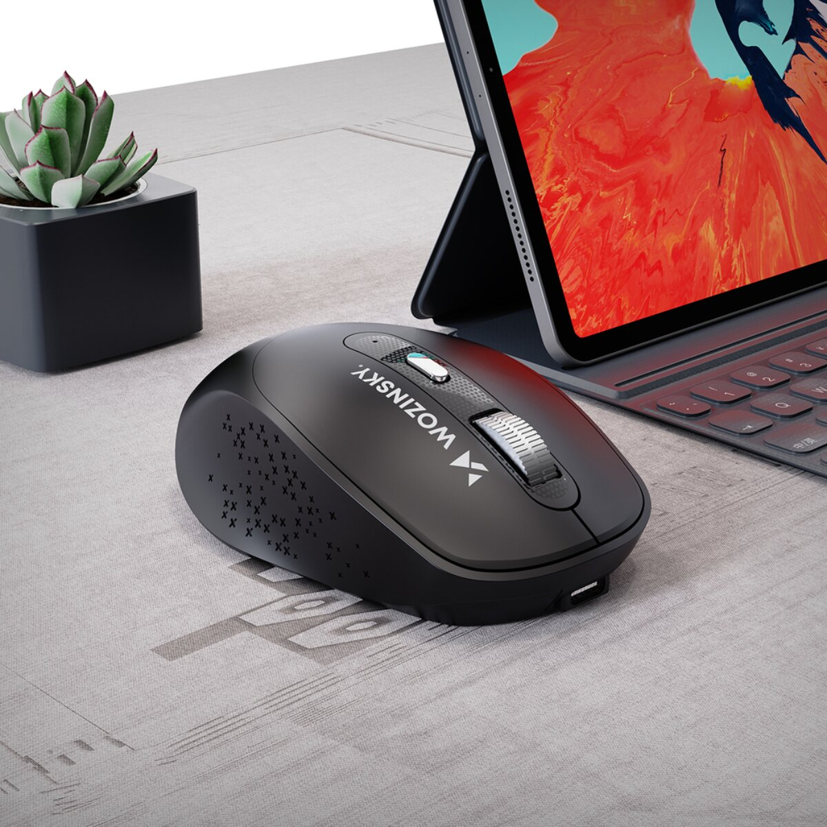 Un mouse per computer nero su una scrivania strutturata accanto a un tablet e una piccola succulenta.