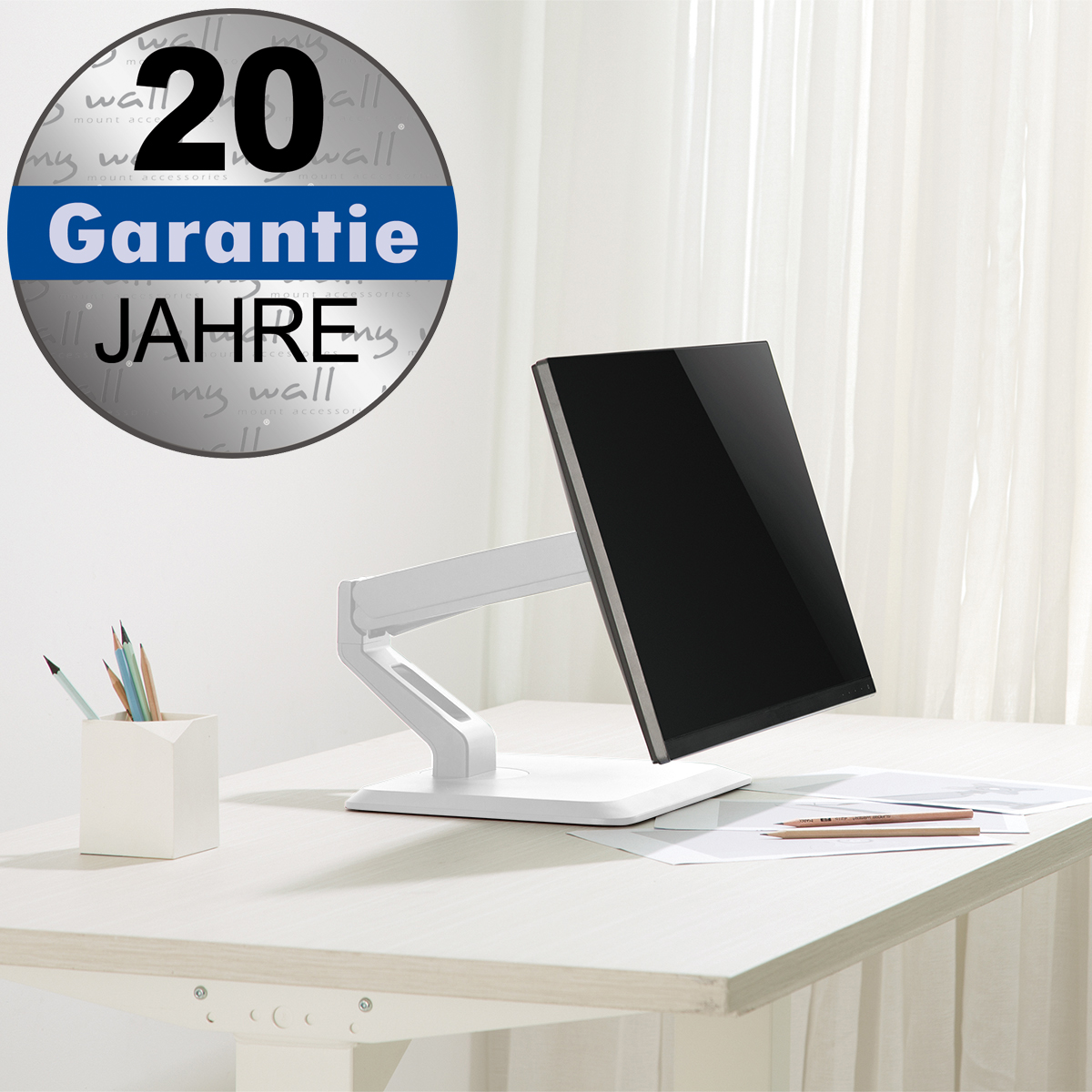 Una scrivania bianca con monitor su supporto, portapenne e fogli.