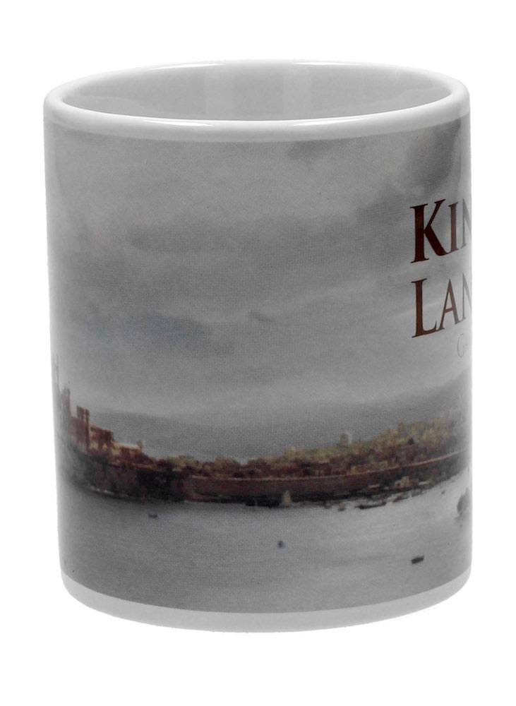 Eine weiße Keramiktasse mit dem aufgedruckten Bild einer ummauerten Küstenstadt unter bedecktem Himmel.