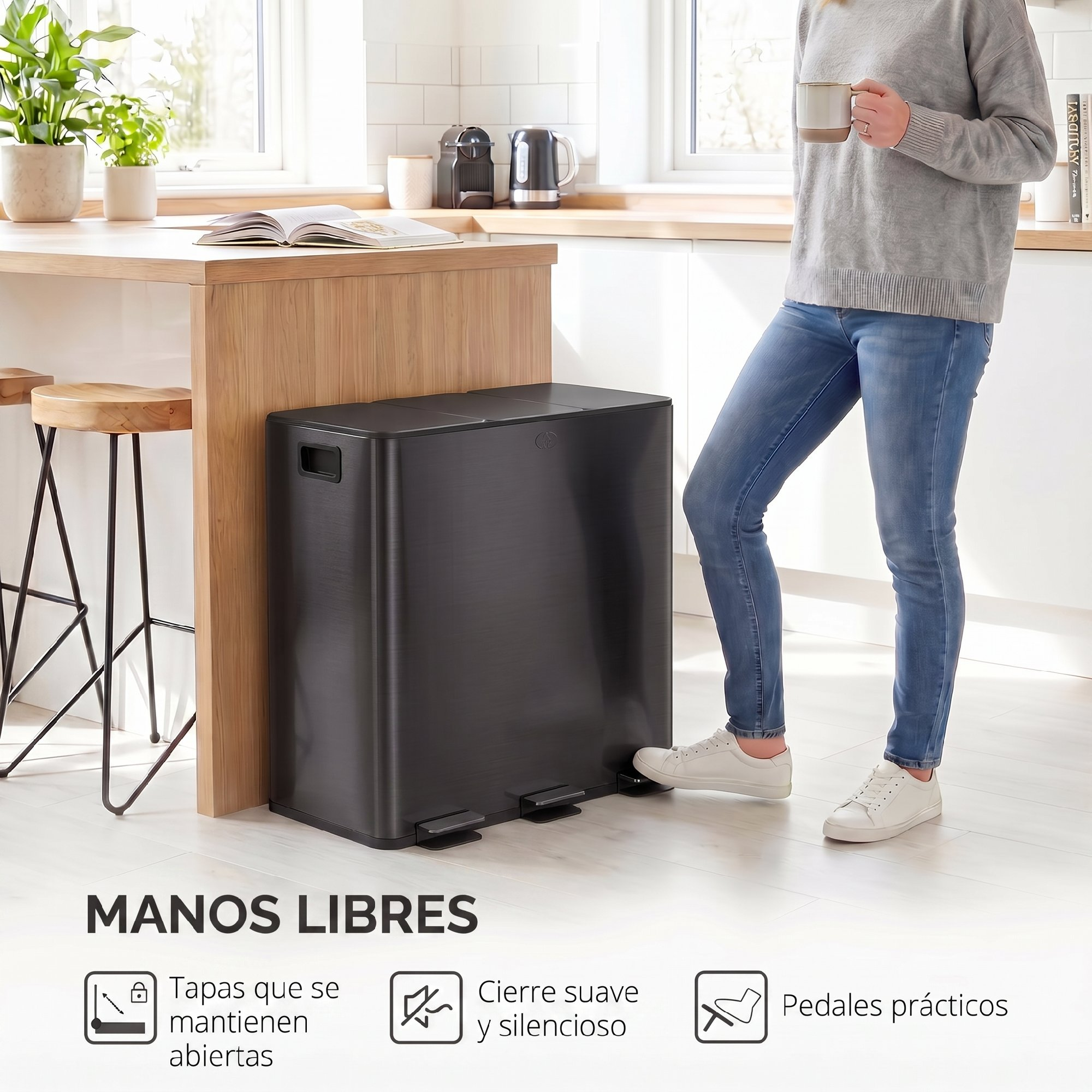 Una mujer con suéter gris y vaqueros pisa el pedal de un cubo de basura negro grande en una cocina.