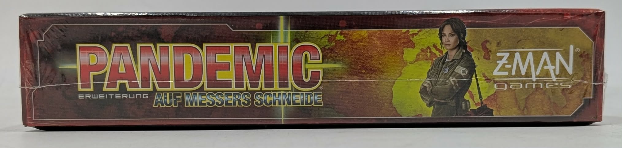 Seitenansicht der Brettspielverpackung 'Pandemic: Auf Messers Schneide' mit rotem Schriftzug und Weltkarte.