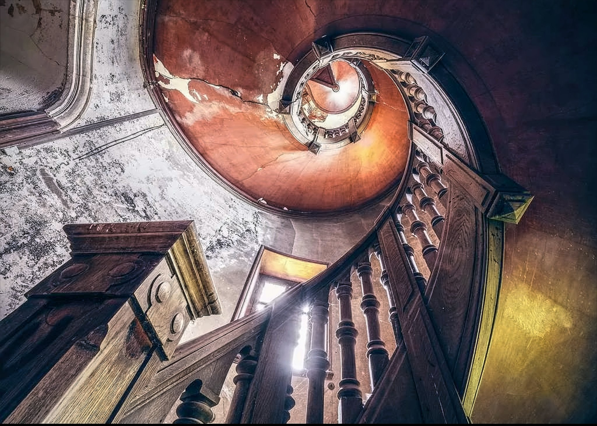 Eine hölzerne Wendeltreppe führt nach oben vor einer rötlichen Decke und verwitterten Wänden.