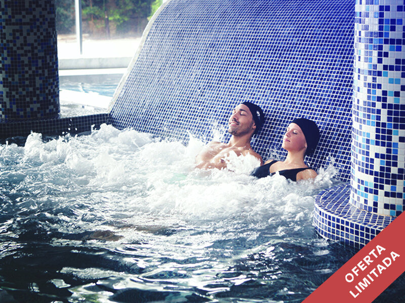 Una pareja se relaja en un jacuzzi con azulejos de mosaico azul y agua burbujeante.