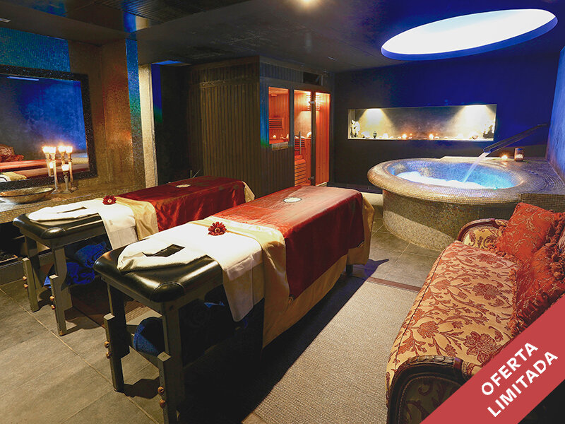 Lujosa sala de spa con dos camillas de masaje, jacuzzi, sauna y un sofá rojo en primer plano.