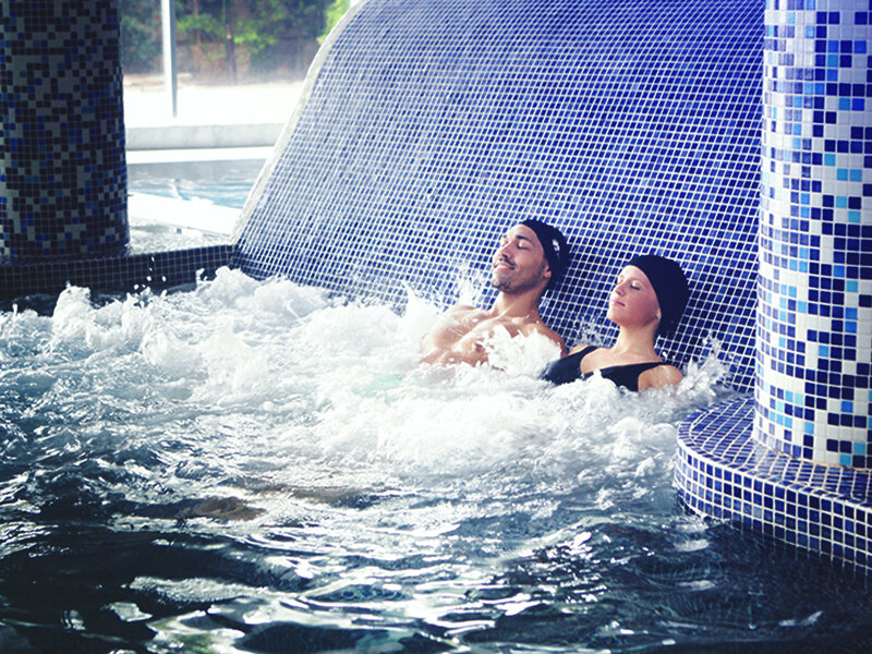 Una pareja con gorros de baño se relaja en un jacuzzi de azulejos azules.