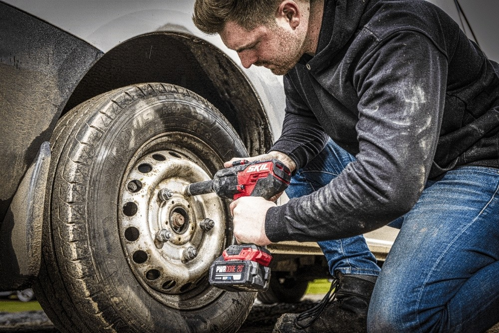 Un mecánico usa una llave de impacto inalámbrica roja para quitar las tuercas de una llanta de auto sucia.